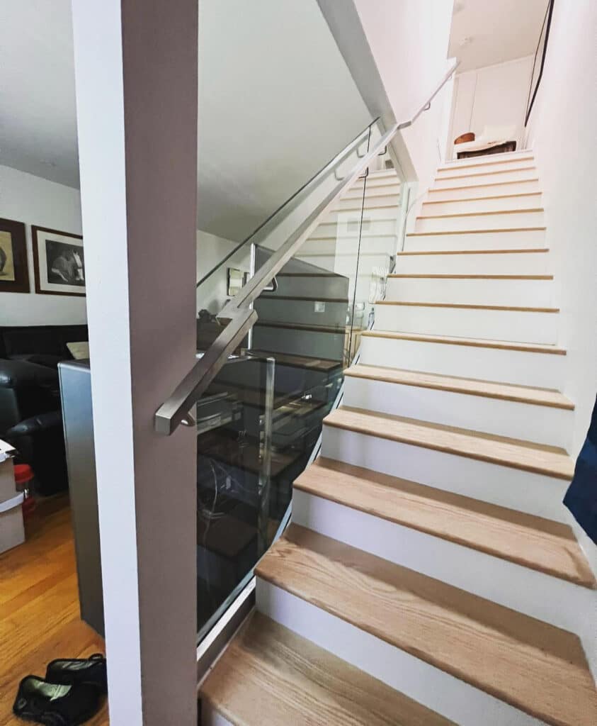Modern staircase with light wood treads and a sleek glass railing system featuring a brushed metal handrail