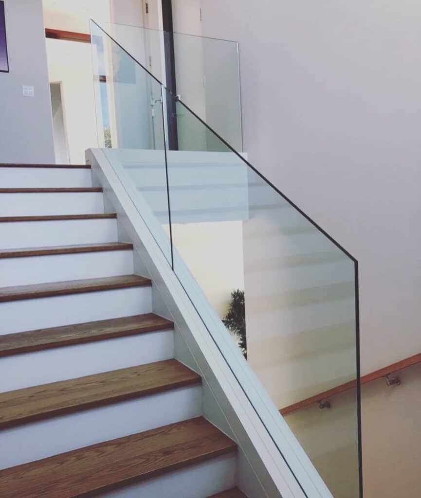 Staircase featuring a clean, minimalist glass railing with no visible frame, paired with white risers and natural wood treads