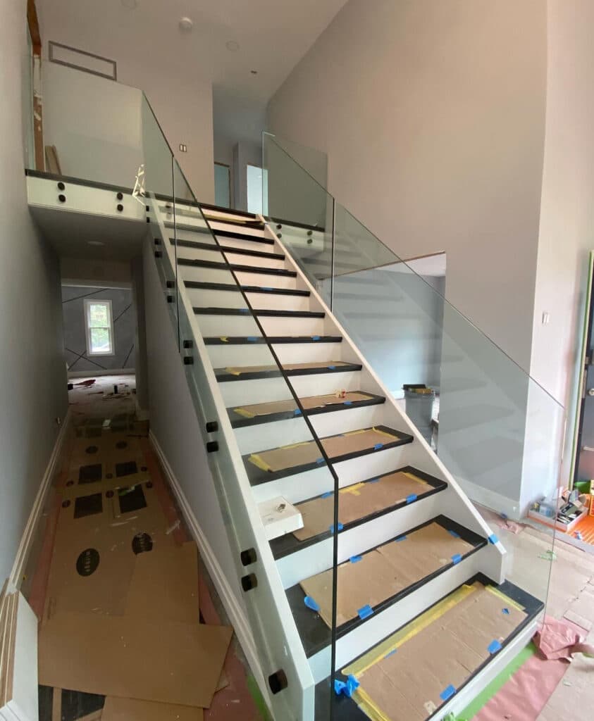 Interior staircase under construction featuring full-height glass railings, designed to add modern elegance