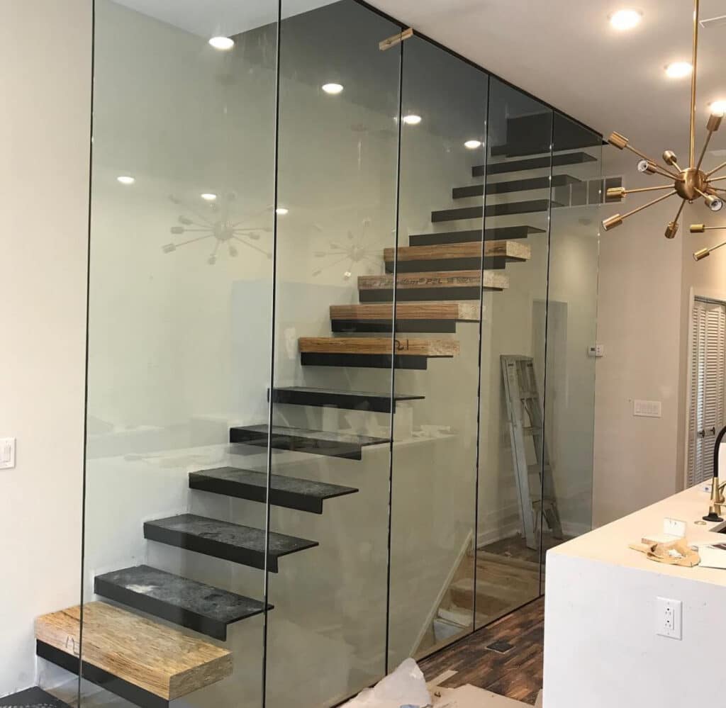 Glass railing system enclosing a modern floating staircase with wood and metal treads, blending safety
