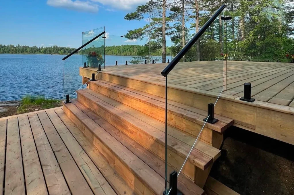 Full glass railing system on deck and stairs overlooking a clean lake and landscaped yard