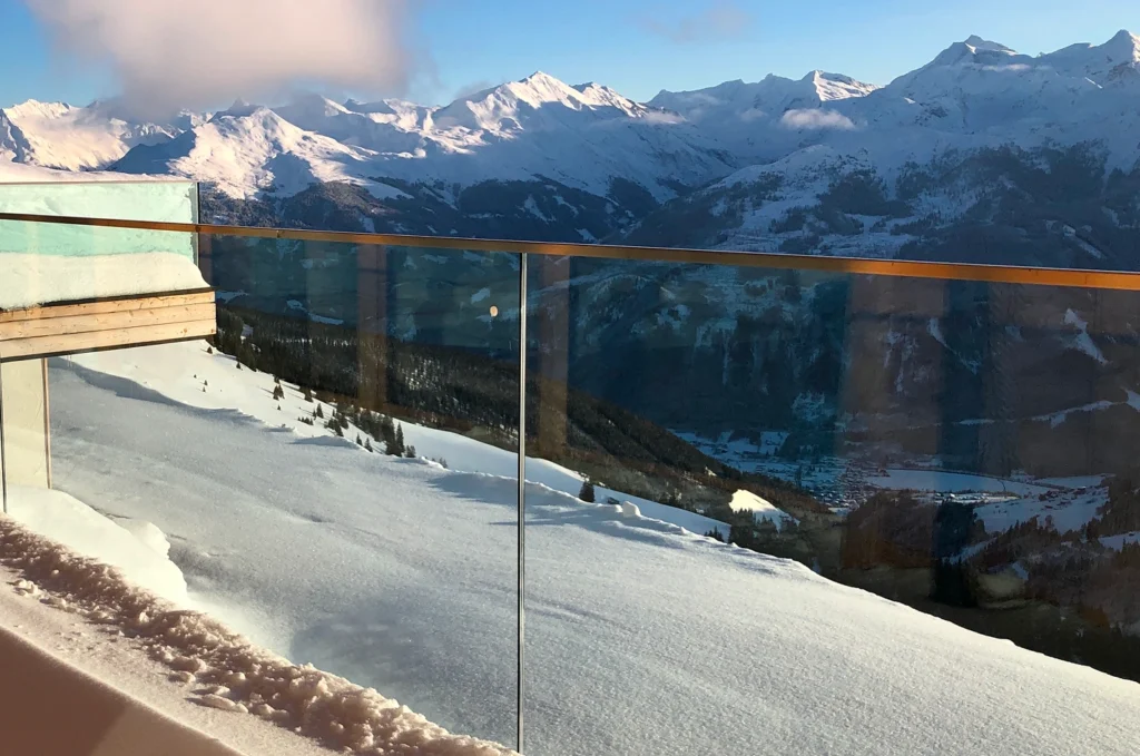 Snow-covered terrace with frameless glass railing at winter resort during heavy snowfall