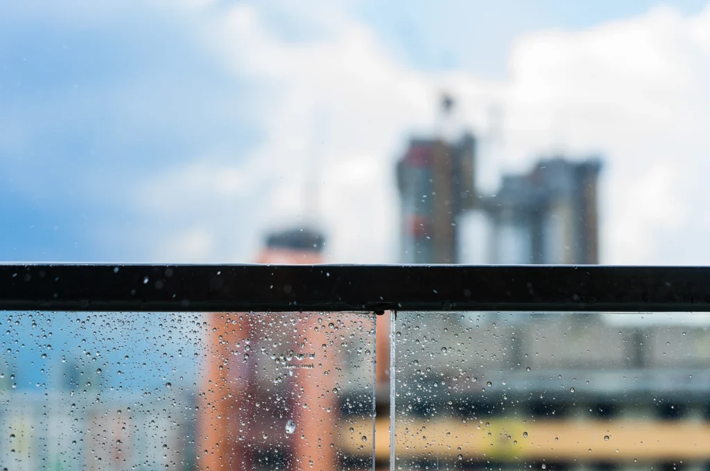 Rainy day view through glass railing on modern balcony overlooking Seattle city and greenery.