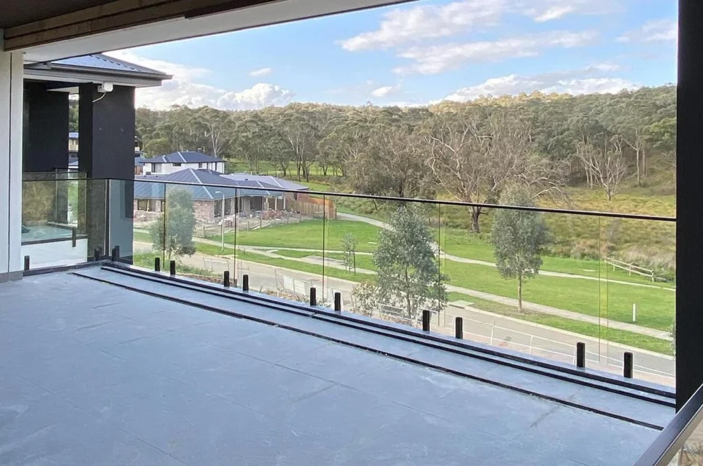 Outdoor terrace featuring frameless glass railing, autumn trees, and residential neighborhood in background.