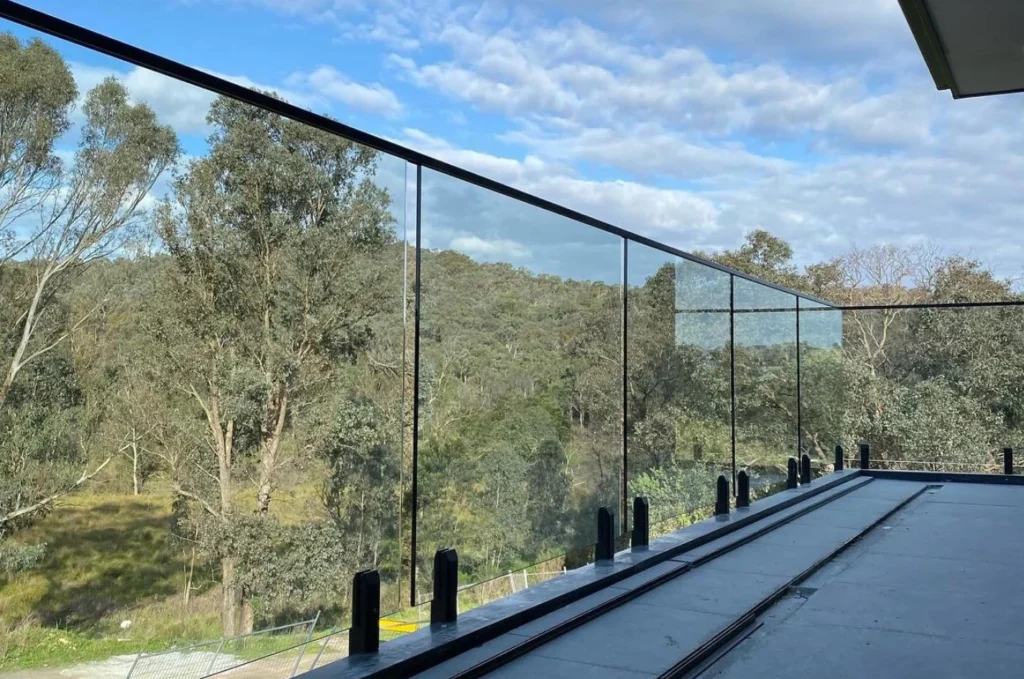 Large terrace with custom frameless glass railing and scenic autumn landscape of green yard and houses
