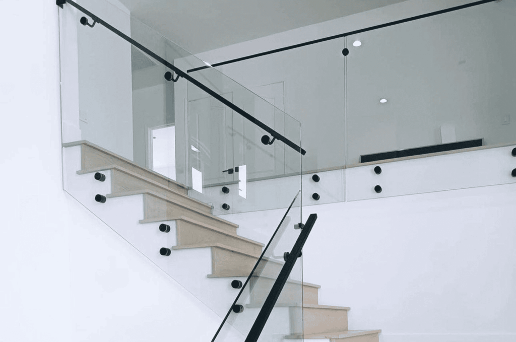 Modern staircase with frameless glass railing hardware with black standoffs and handrail in white interior