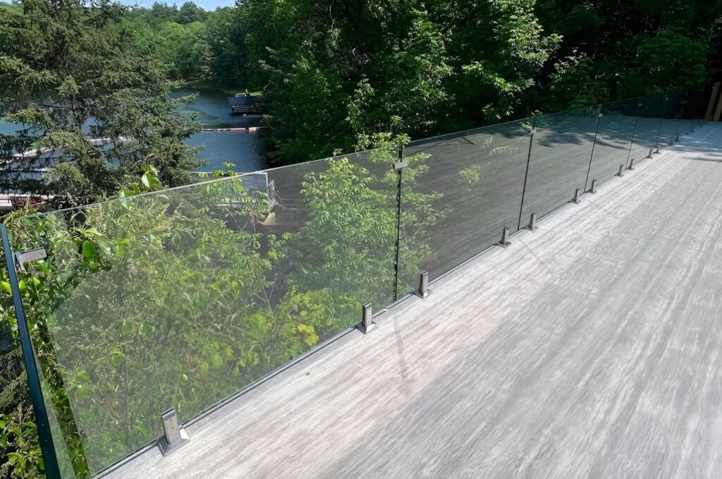 Sunny outdoor view of a residential deck with a clear glass railing, overlooking a yard and open natural scenery, highlighting unobstructed views and modern design.