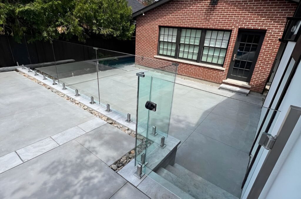 Newly installed outdoor glass balustrades made from high-quality materials, enclosing a residential yard and pool area and lining exterior stairs, providing safety with clear, modern views.