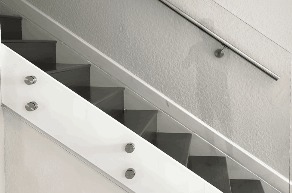 Standoff mounted indoor glass railing on staircase, showing side-mounted bolts and minimalist handrail design