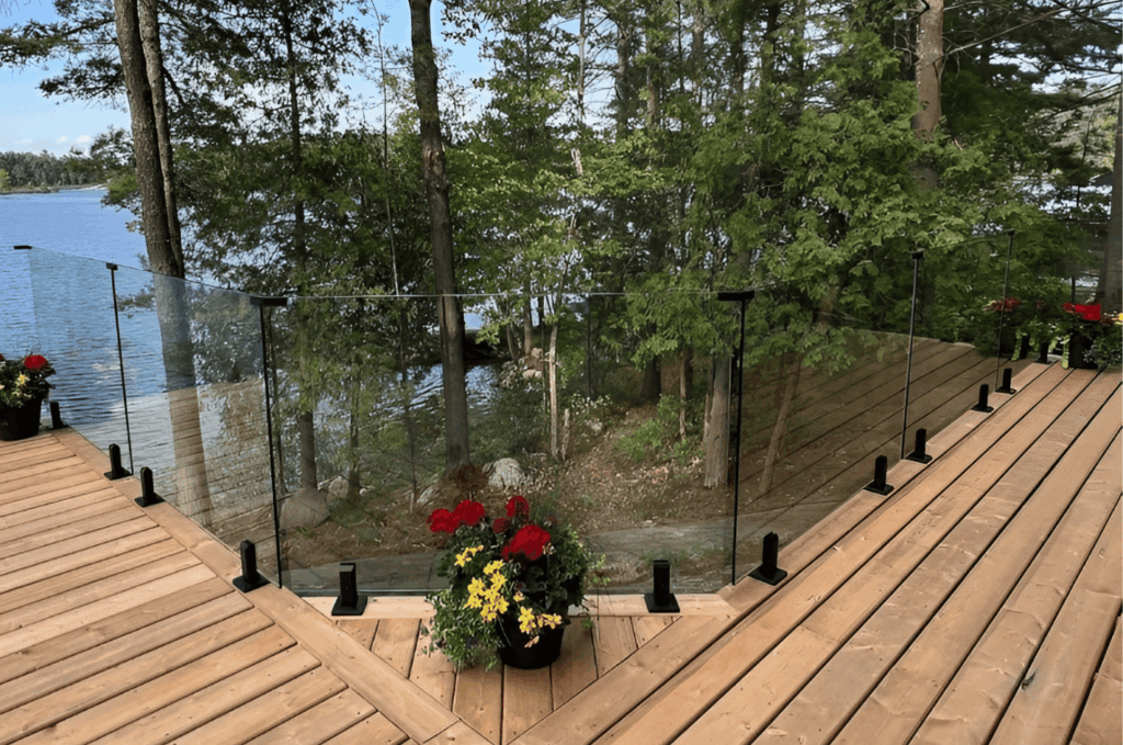 Outdoor deck with clear glass railing overlooking lake, showcasing elegant glass railing design trends