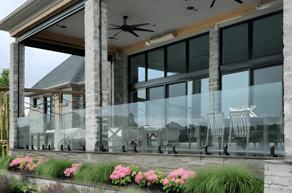 Commercial glass railing enclosing an outdoor patio terrace with stone columns, seating area, and garden view