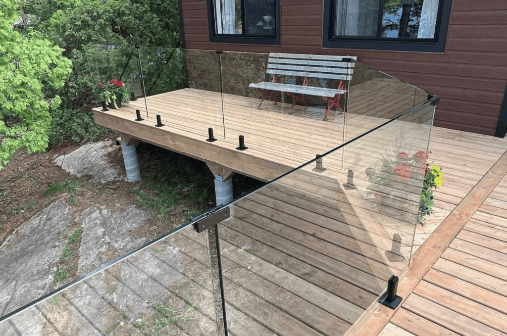 Deck for glass railing installation with clear panels and stainless posts around a modern wooden platform.