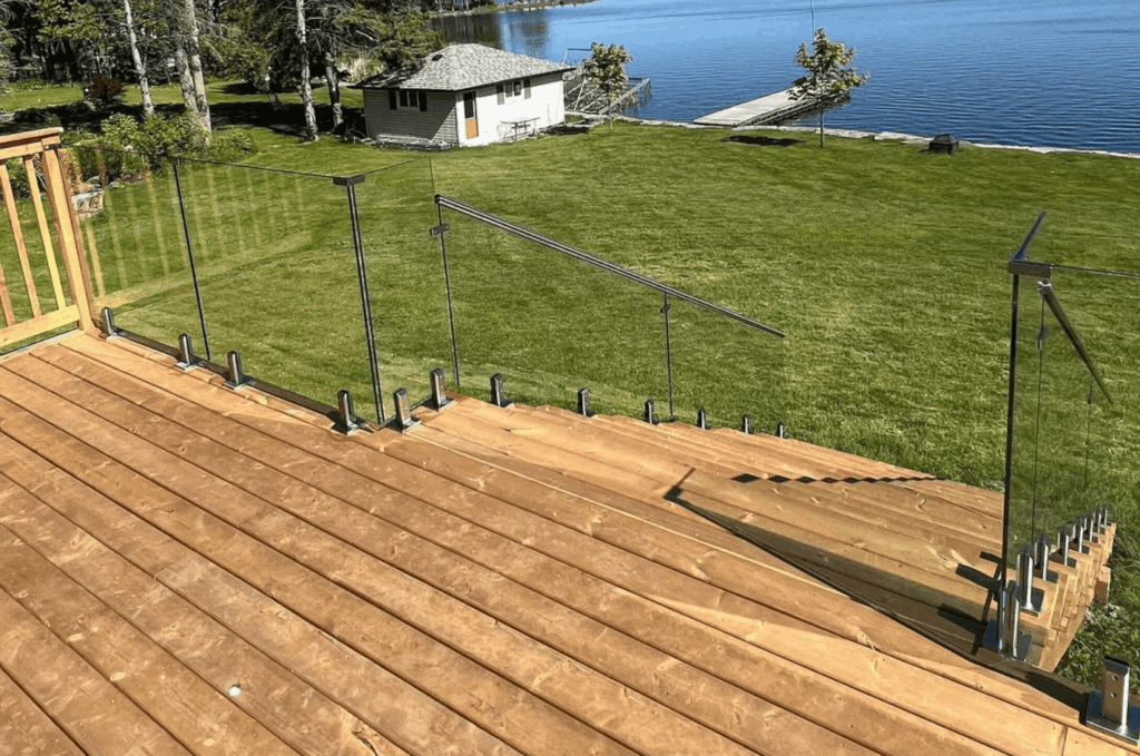 Deck for glass railing installation overlooking a waterfront backyard with stainless steel posts and clear glass panels.