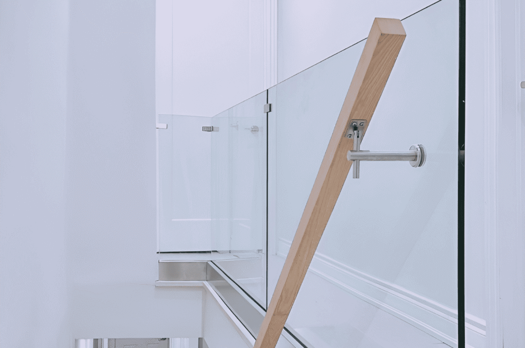 Close-up of frameless glass railing installation with wood stair support and stainless steel hardware