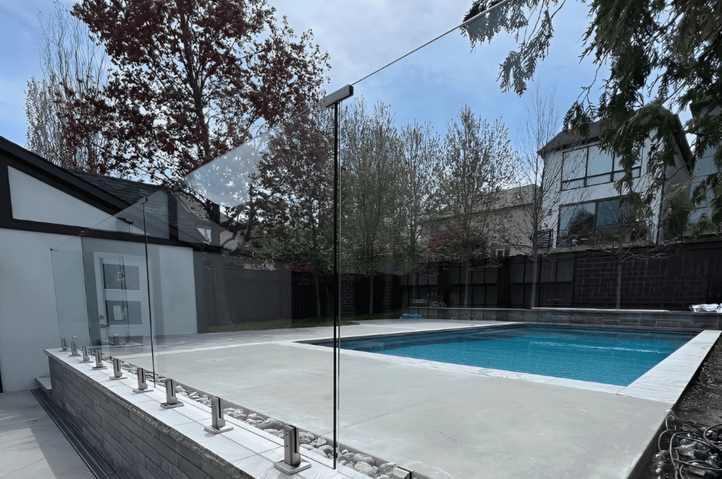 Modern backyard pool area with clear glass railing panels for safety without blocking the view 