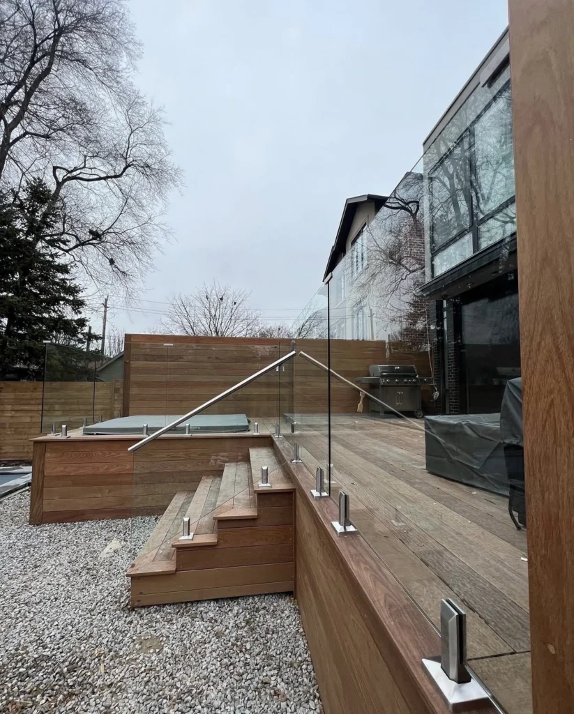 Raised wood outdoor deck installed with sleek glass deck railing along the stairs and upper seating space