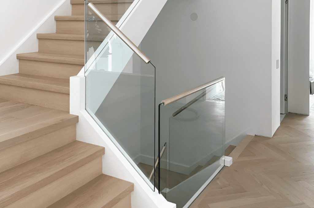 Wooden staircase with a clear glass stair railing and metal handrail, creating a safe, open, and modern interior look.