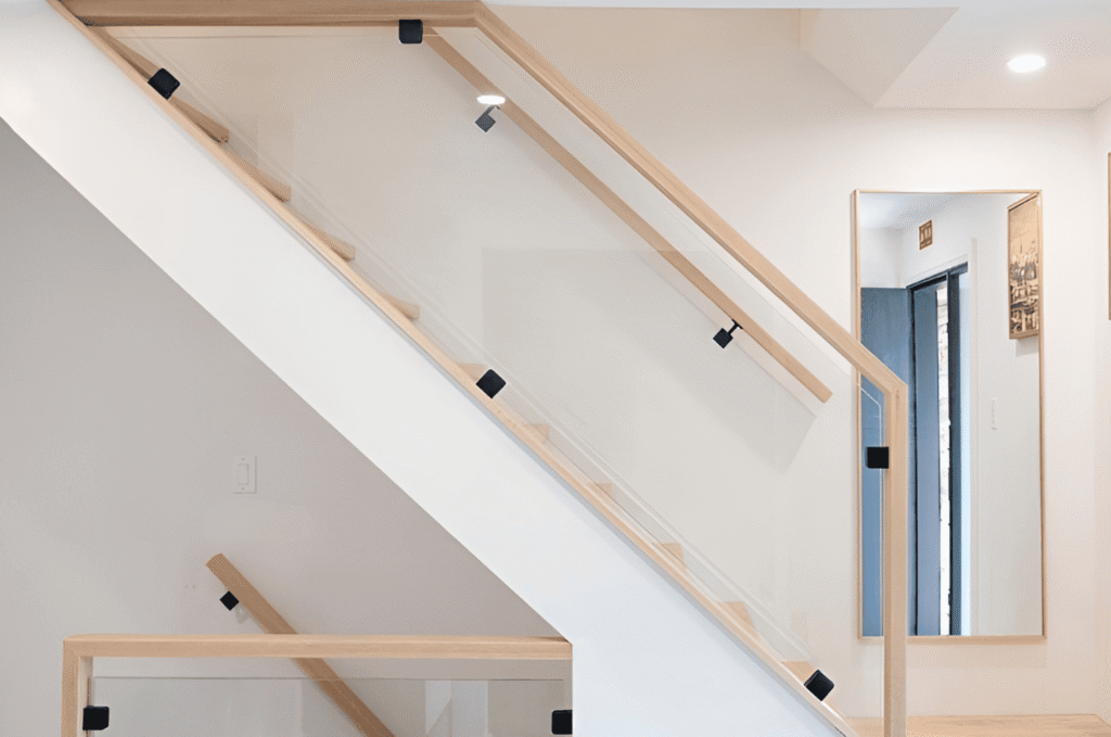 Modern staircase with premium glass railing systems and wood handrail, creating a clean, open, and high-end interior look.