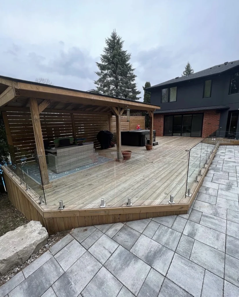 Spacious backyard outdoor deck install featuring frameless glass deck railing around the wood platform and patio area