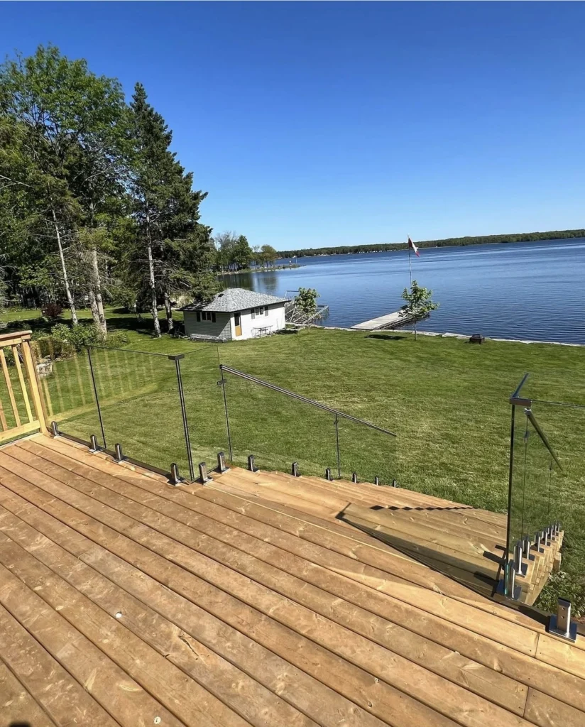 Lakeside wooden deck with clear glass deck railing, part of a clean and modern outdoor deck installed overlooking the water