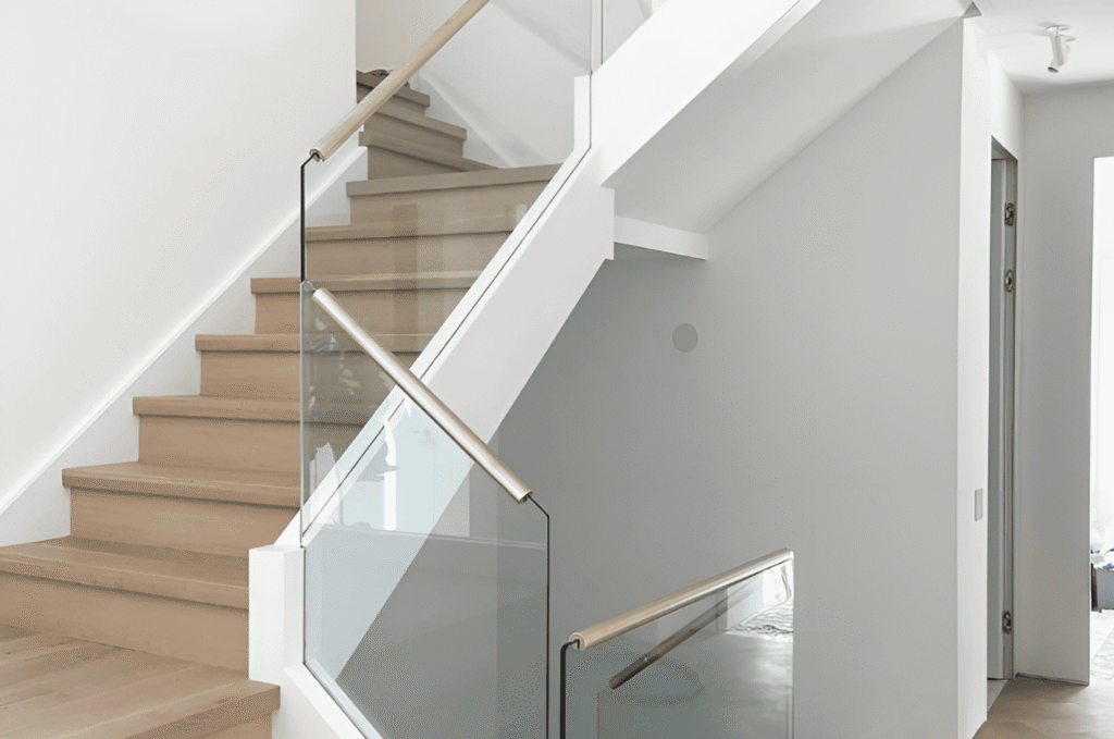 Modern indoor staircase with clear glass railing and light wood steps creating a bright, open look.