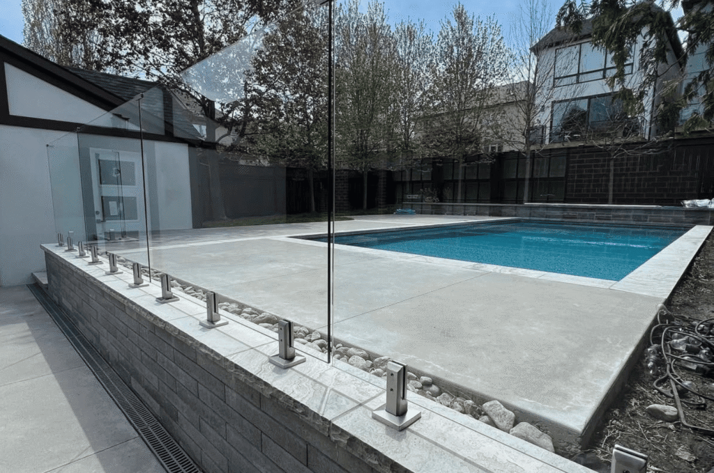 Backyard pool surrounded by a modern outdoor glass railing for safety and clear views