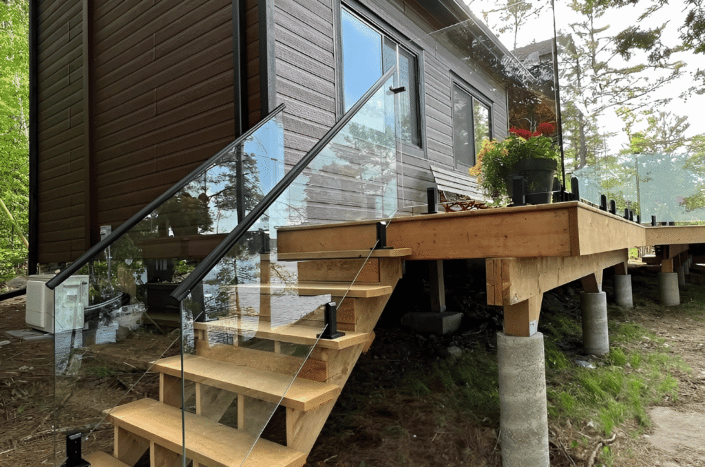 Wooden deck with stairs and a clear outdoor glass railing beside a lakeside home