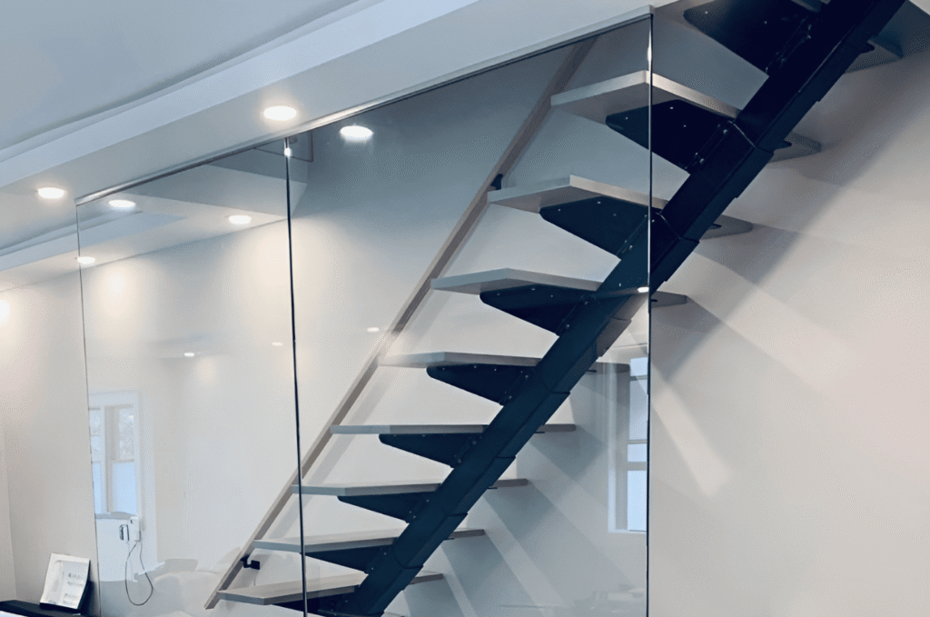 Frameless glass stair railing installed alongside a modern floating staircase with a black steel frame in a Seattle home interior.