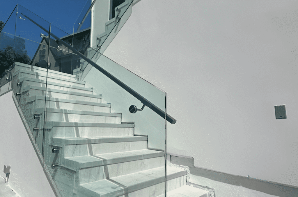 Outdoor glass stair railing with standoff clamp hardware and a stainless steel handrail installed on marble steps at a Seattle residential property.