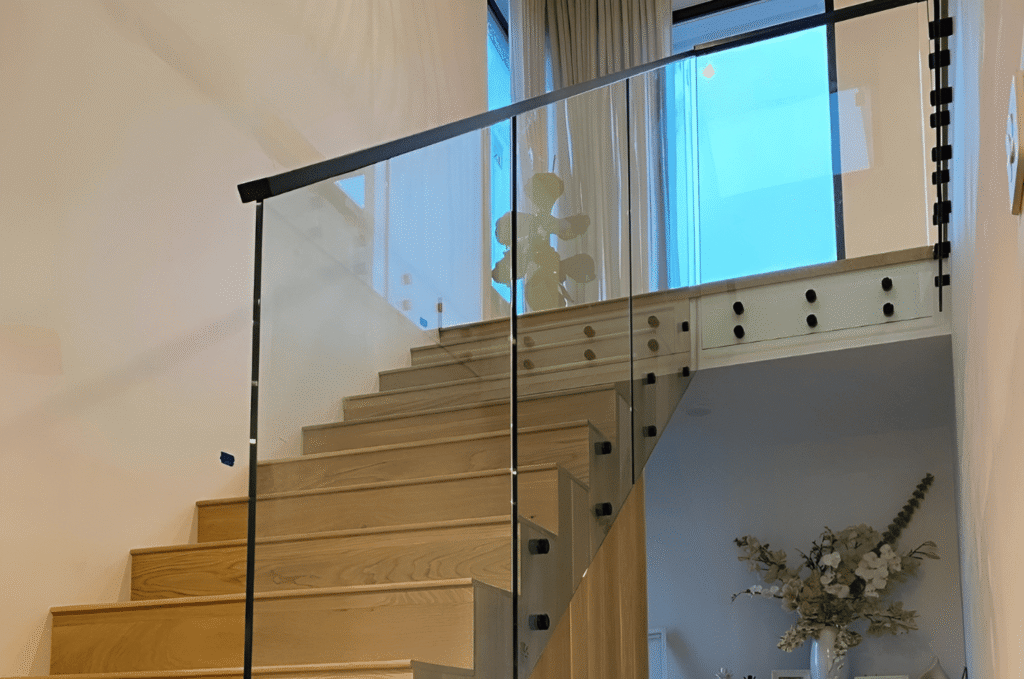 Indoor wooden stairs with a framed glass railing and dark metal frame, offering durability and a stylish finished look