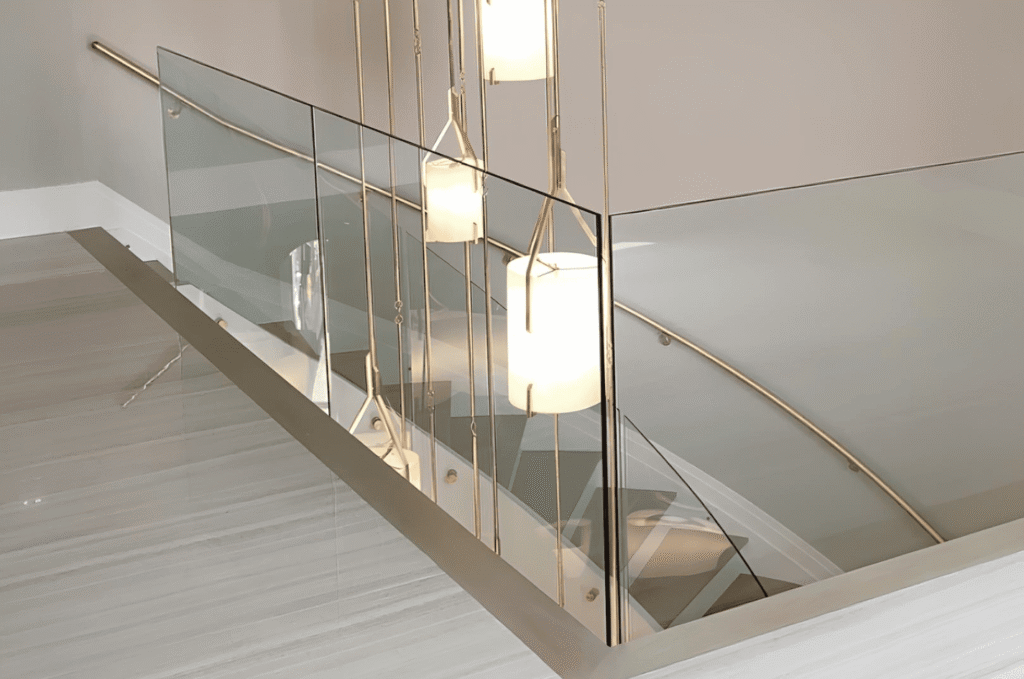 Semi-frameless glass stair railing with metal handrail and tempered glass panels meeting glass railing safety standards 