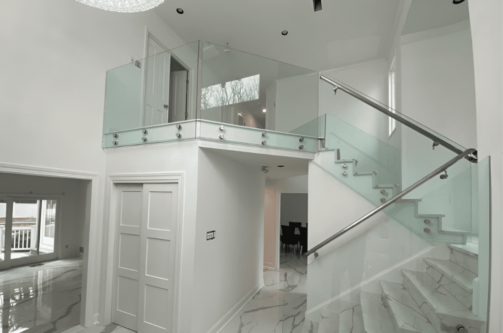 Frameless glass balcony and stair railing with stainless steel standoff hardware in a bright two-story Seattle home interior.