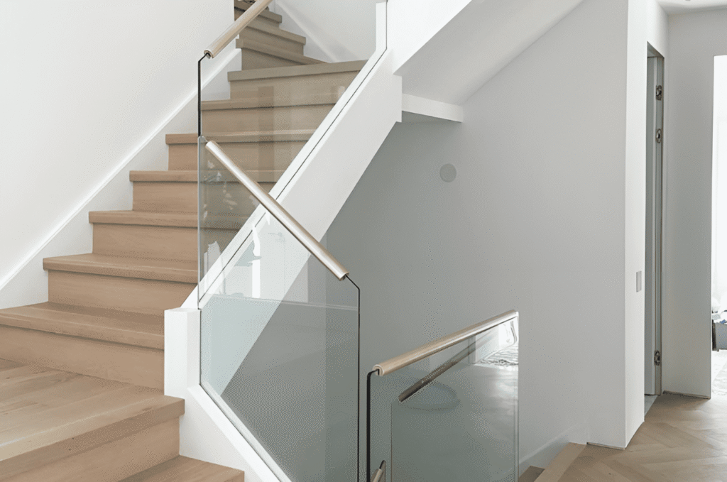Frameless glass stair railing with gold handrail installed on oak steps after design approval was completed