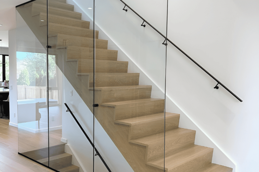 Full-height glass stair railing with black hardware and oak steps showing precise panel alignment after design revisions