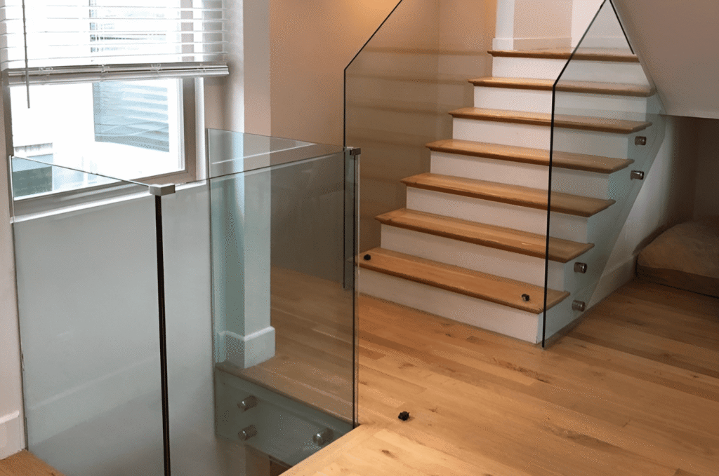 Frameless glass railing with standoff mounts along a wooden staircase ready for final inspection and walkthrough