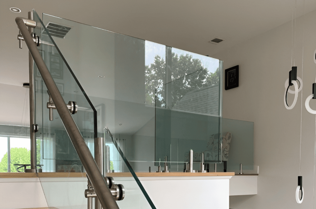 Interior frameless glass railing with stainless steel standoff clamps and a brushed handrail on a modern home staircase. 