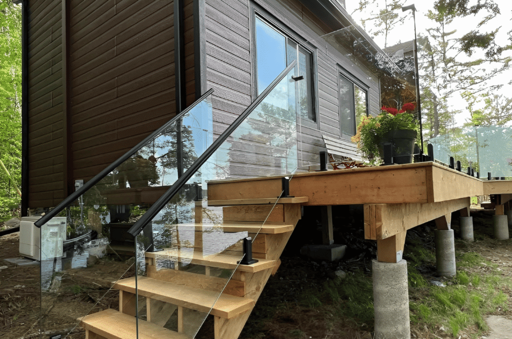 Frameless glass stair and deck railing with matte black post hardware on an elevated wood cabin exterior.
