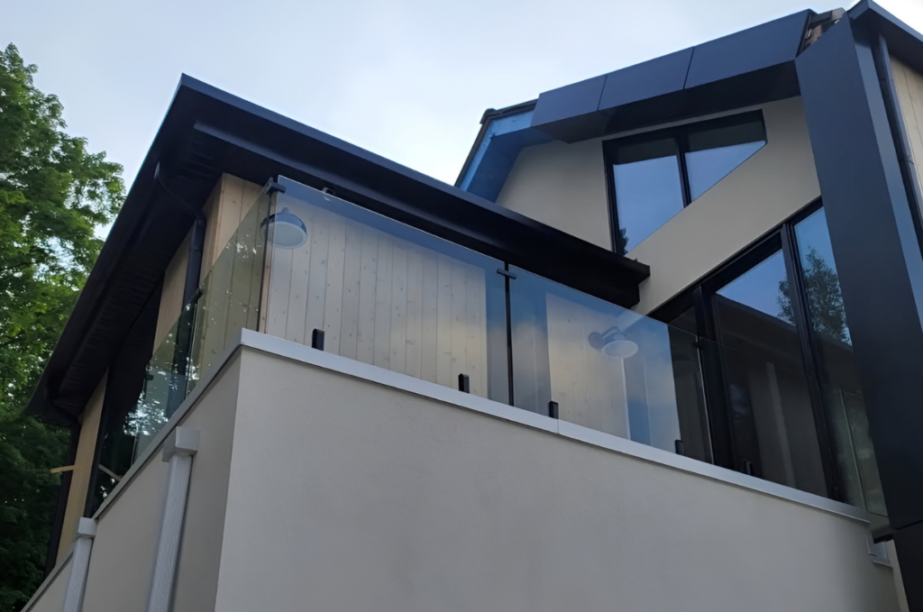 Tinted frameless glass balcony railing panels installed across multiple floors of a modern white residential building.