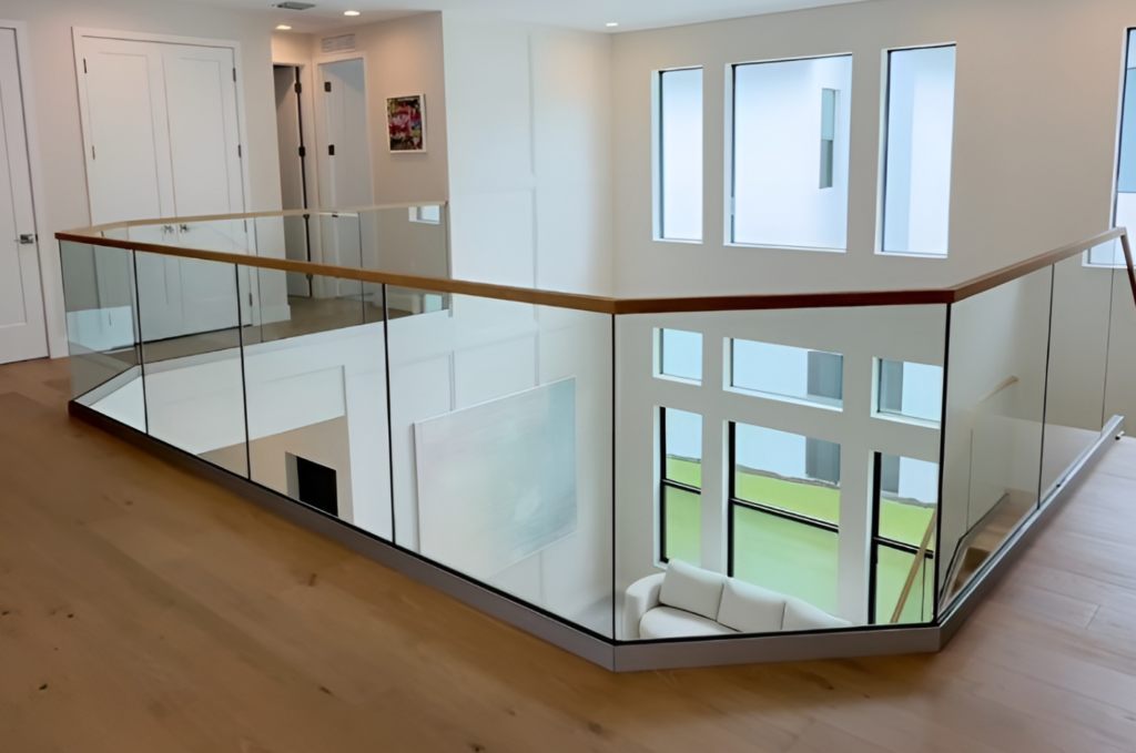Professional glass railing installation with clear panels, wood handrail, and upper-level walkway in a bright modern home 