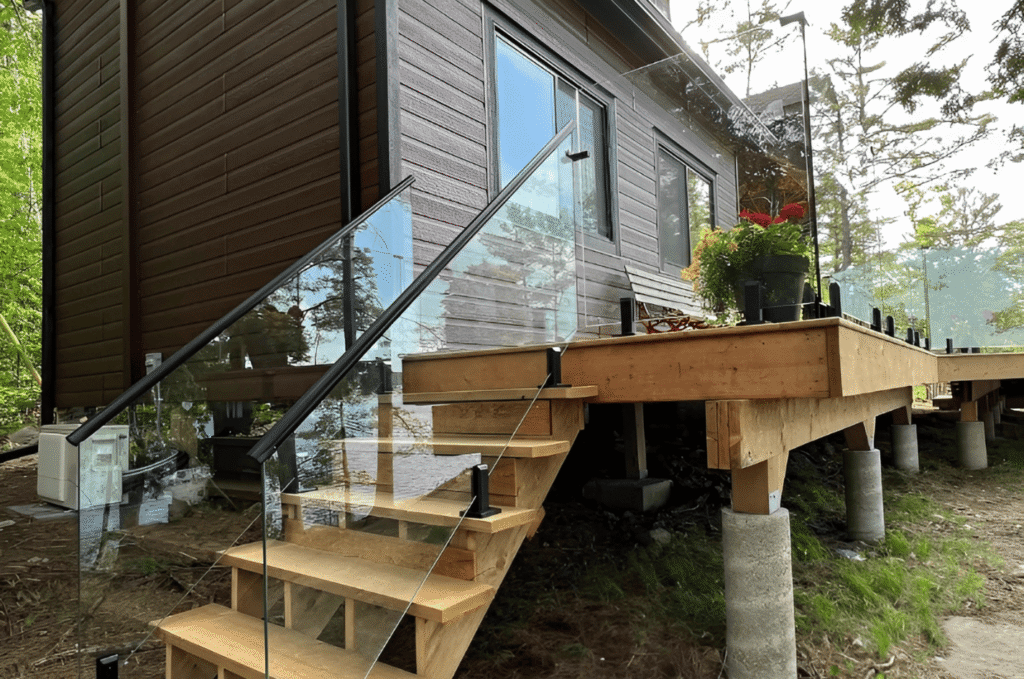 Custom glass railing installation on outdoor deck stairs with clear panels, black posts, and natural wood framing near home 