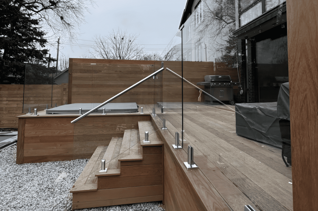 Glass railing panels secured in base channel hardware during professional installation with standoff mounts on a Seattle deck