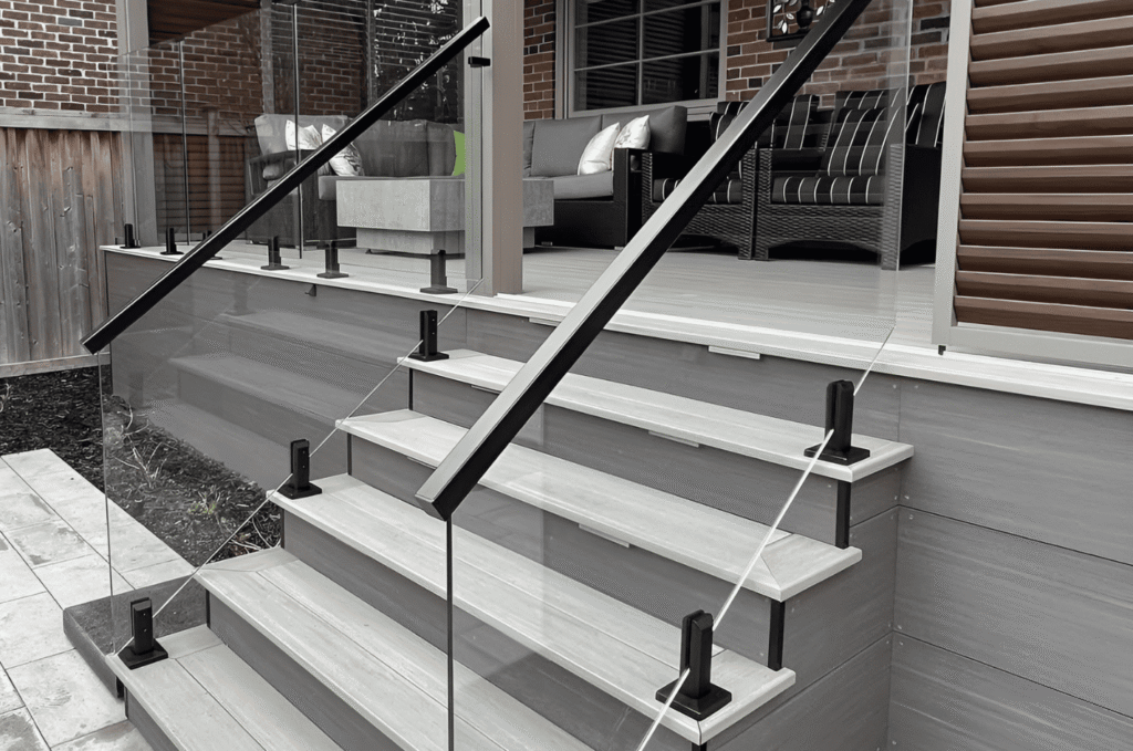 Completed outdoor glass stair railing installation with black standoff hardware and frameless panels on composite deck steps
