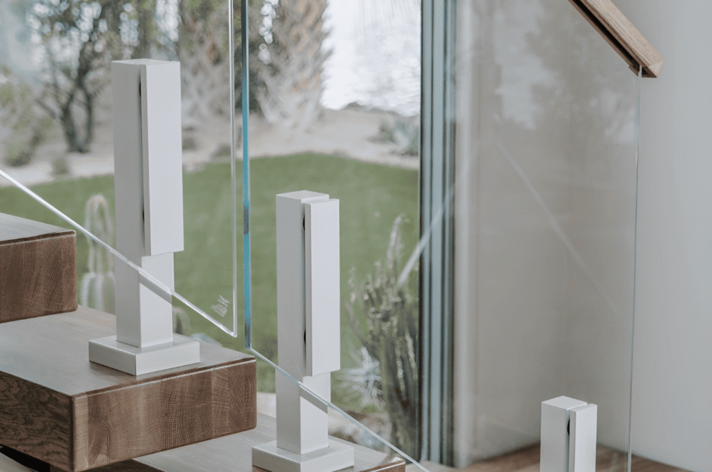 White glass railing spigots holding clear panels beside wood stairs, showing subtle frameless hardware in a modern interior.