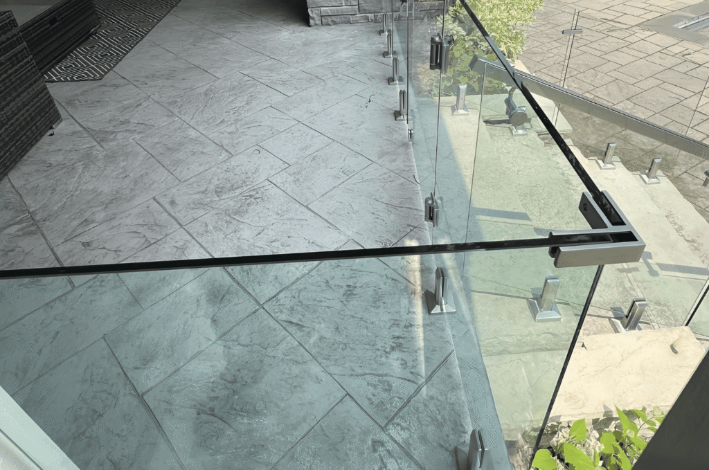 Glass stair railing hardware shows aligned clear panels, metal clamps, and top rail connections on an outdoor tiled landing 
