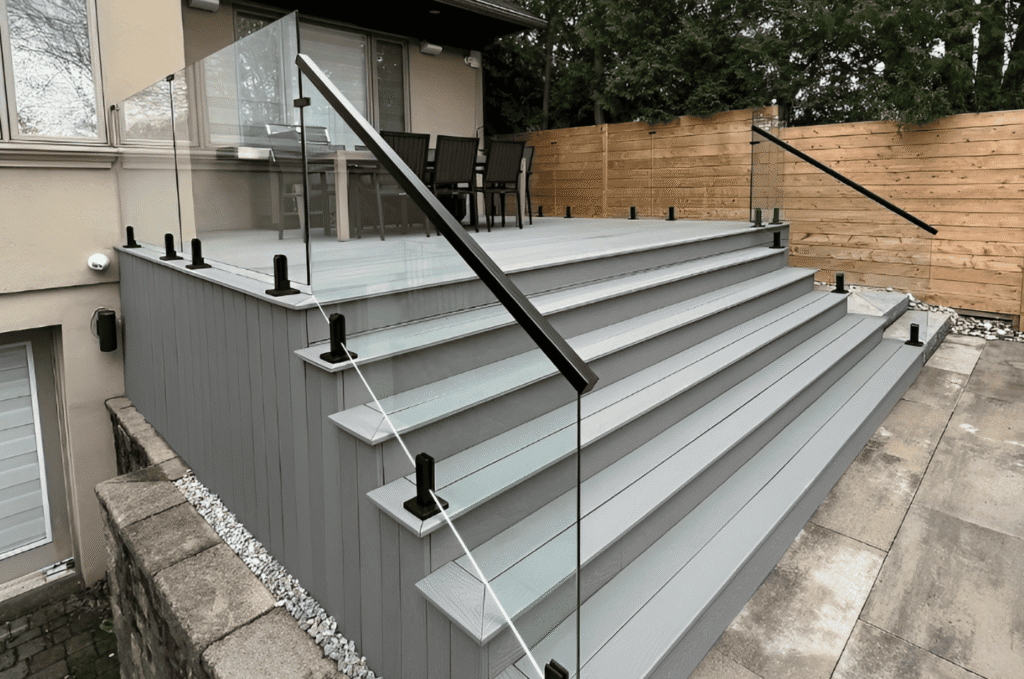 Custom glass deck railing with matte black posts framing a wide outdoor staircase on a modern residential home 