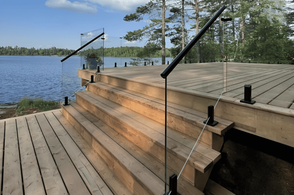 Residential custom glass railing system with matte black top rail installed on a lakeside cedar deck and staircase 