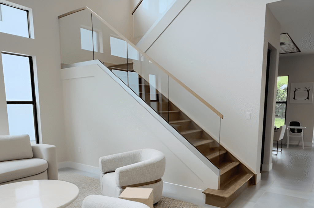 Frameless glass stair railing with wood handrail in modern home interior requiring protection during renovation and painting