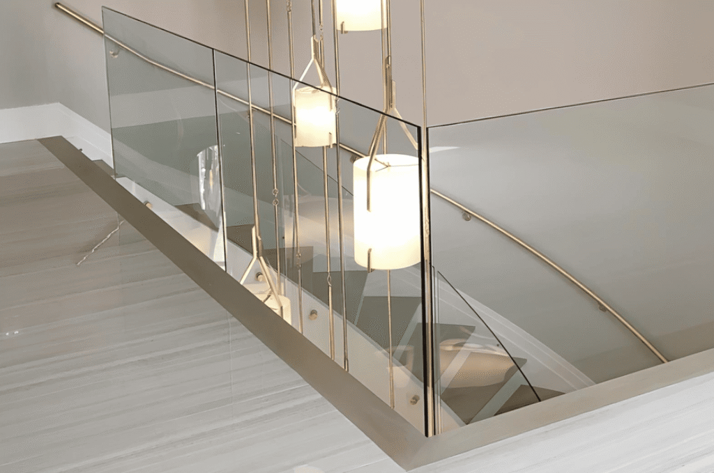 Indoor frameless glass loft railing with gold hardware and pendant lights needing regular summer glass railing cleaning care