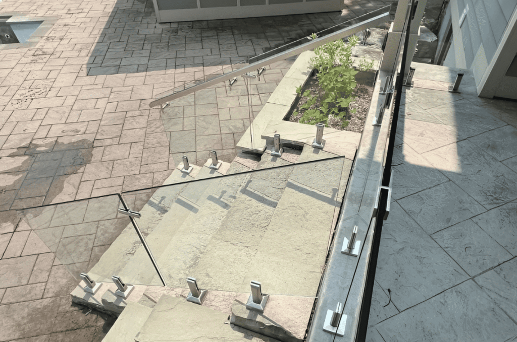 Tempered glass deck railing panels held by stainless steel spigot hardware on a stone outdoor patio near a Seattle home