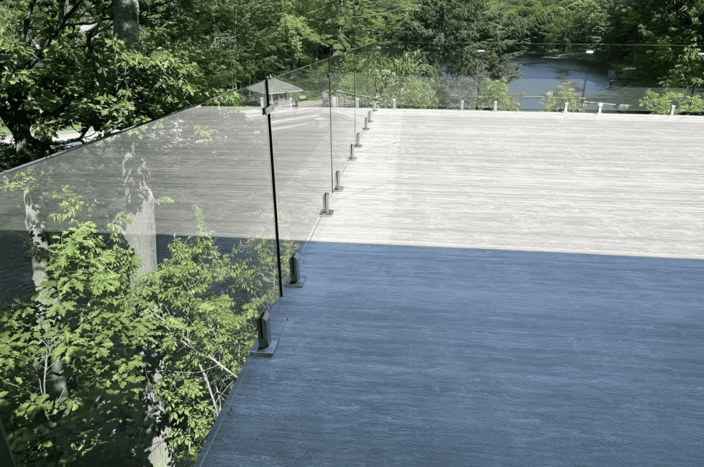 Frameless glass deck railing with base shoe hardware on stone terrace showing custom deck glass railing design and open view